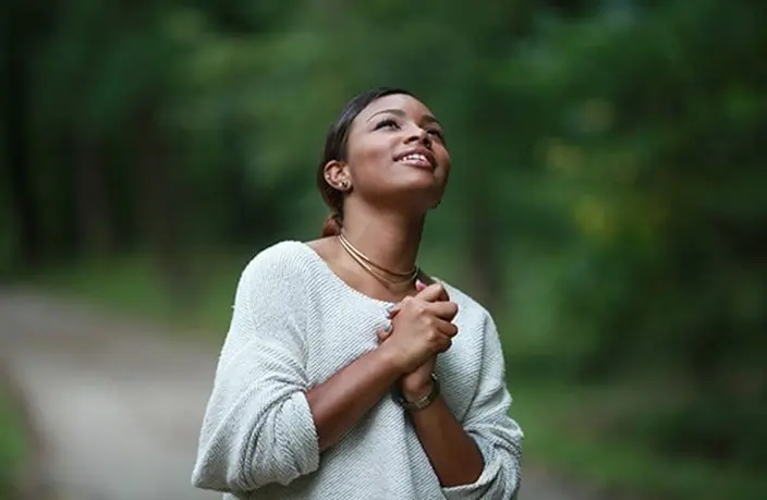 A woman is praying outside in the woods.